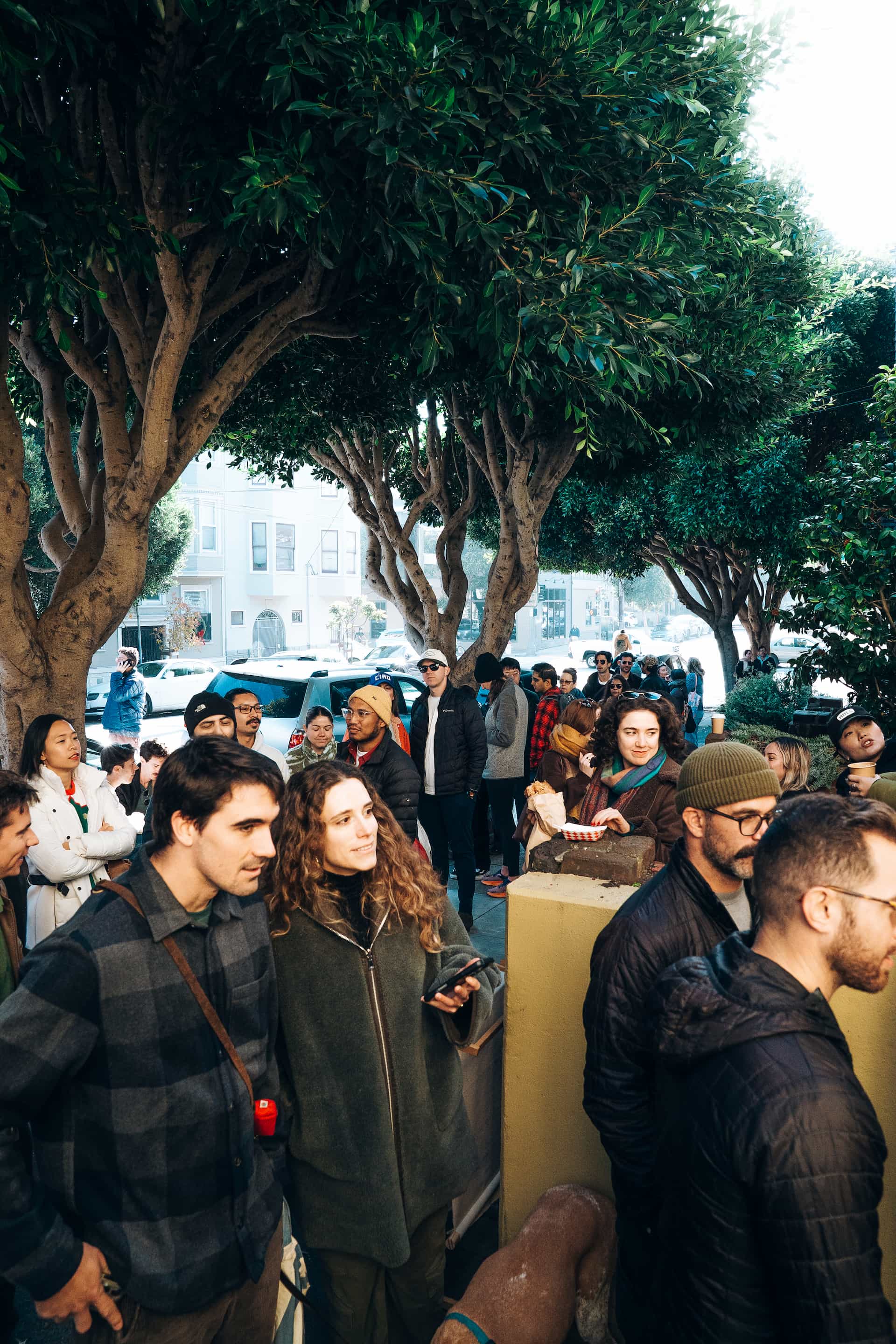 The crowd at a blue house coffee event in san francisco. Trees line the sidewalk in the background.